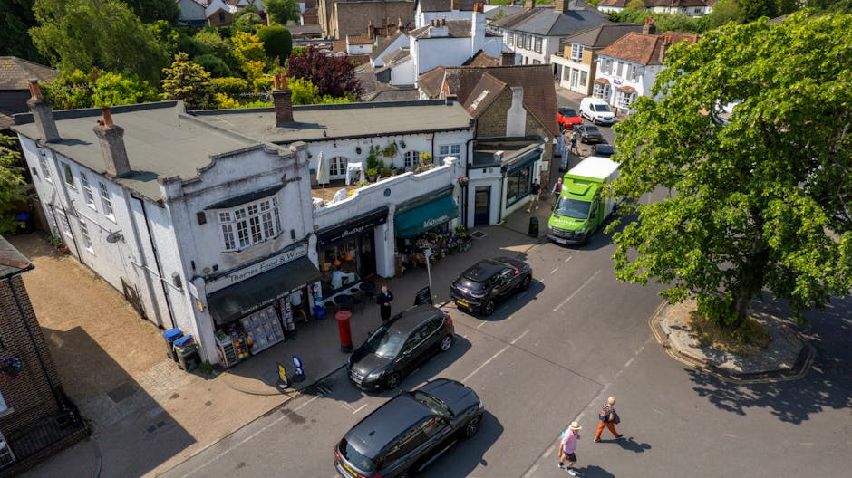 An aerial view of a street scene in Chiswick High Road with a small florist shop, Flowers in Bendel, featuring a white building with teal awnings and a display of floral arrangements outside. Several 